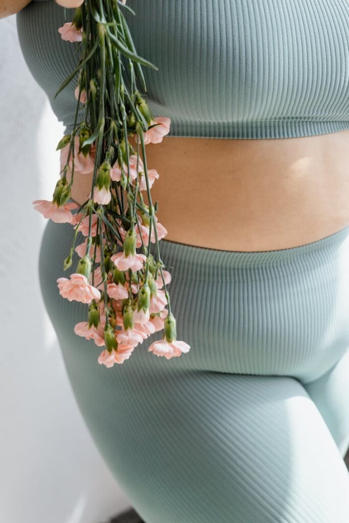Close-up of a plus-size figure in a ribbed workout set holding pastel pink flowers, exuding elegance.